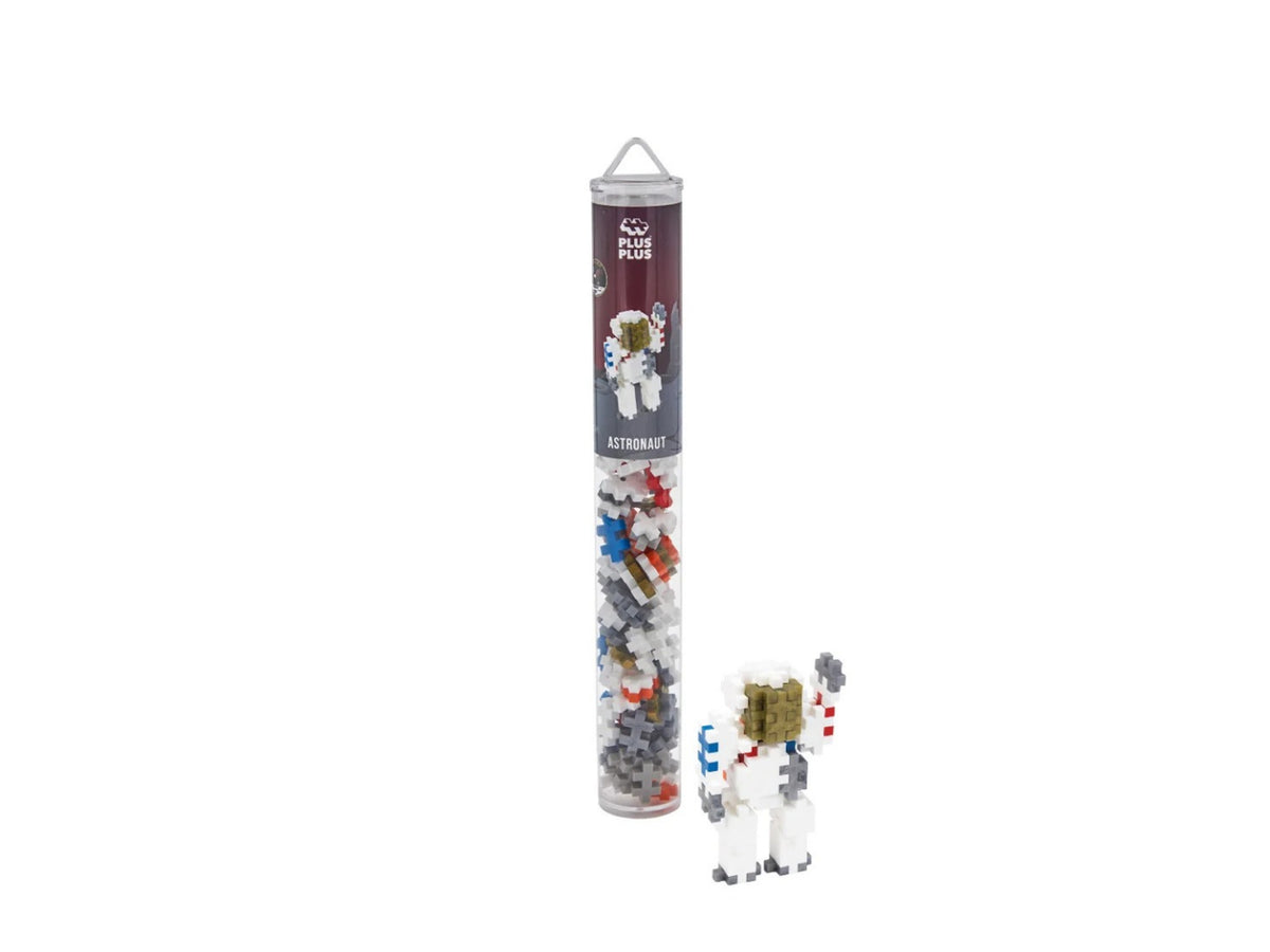 A small astronaut toy shown next to its clear cylindrical storage tube on a plain white background. The tube has a dark label with an astronaut illustration and the text 'ASTRONAUT'.