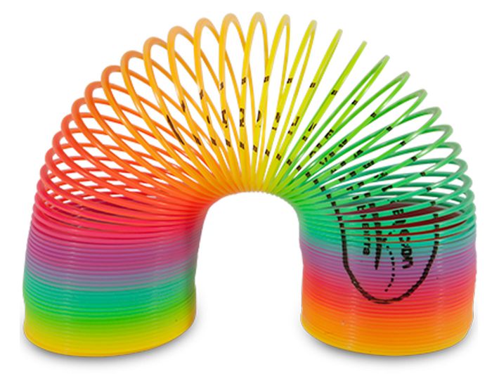 Plastic spring toy, known as a Slinky, displayed in an arched position. The coils transition through a rainbow gradient of colours