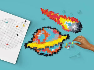 A colorful jigsaw puzzle set displayed on a bright blue background, showing a partially assembled space-themed puzzle with a planet and comet, a white puzzle sheet with black outlines, and a person's hand placing small pieces.